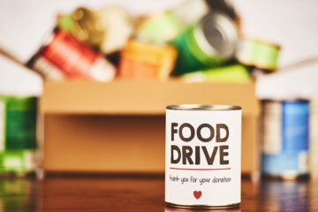 Canned goods in a box for a food drive. Can in front advertises food drive.
