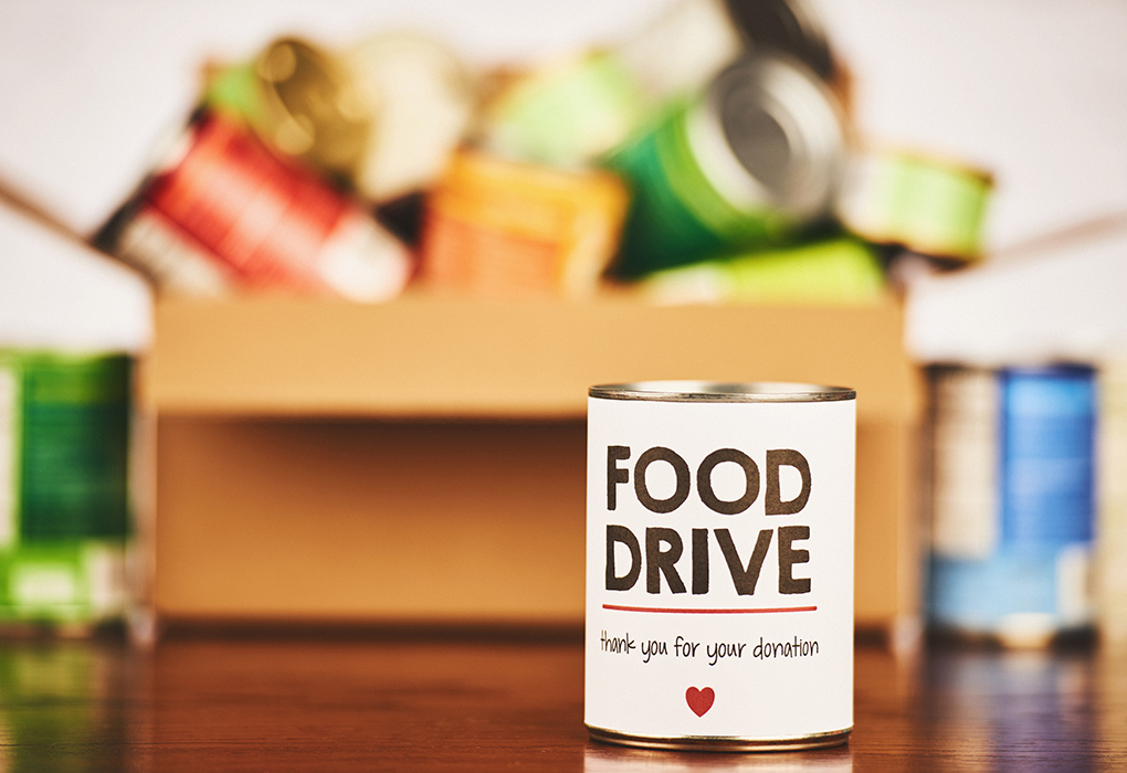 Canned goods in a box for a food drive. Can in front advertises food drive. 